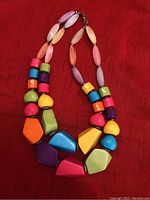 Photo of an 18-inch chunky bead necklace with various bright colored geometric beads arranged on a red fabric background.