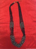 Front view of multi-strand beaded necklace laid flat on red background, showing black and white bead arrangement and clasp with adjustable chain.
