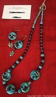 Photo of handmade turquoise necklace with painted floral pendants and matching earrings on red fabric