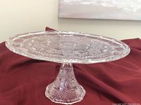 Side view photo of clear glass or crystal pedestal cake stand showing detailed patterned surface and textured pedestal base.