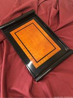 Rectangular wooden serving tray with black lacquer edges and an orange decorative center, placed on a red fabric background.
