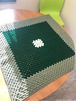 Crocheted blanket laid flat on table showing full size and color pattern of white center, dark green middle, and light green border.