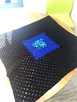 Full view of the crocheted blanket laid flat showing black background and blue multi square center pattern.