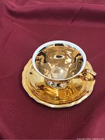Gold small teacup and matching saucer with reflective gold finish and rose detail on the side of the cup