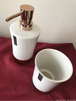Close-up photo showing white ceramic liquid soap dispenser with rose gold pump and matching cup with rose gold base, stickers visible