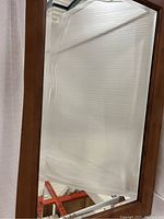 Mirror with rectangular caramelized wood frame and visible crown detail at the top, reflective surface shows white backdrop and light.