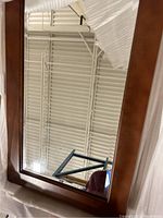 Front view of one 24 inch wooden framed mirror showing frame detail and reflection of ceiling and objects.