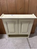 Front view of the antique white medicine cabinet showing two doors and an open shelf below.