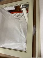 Close-up photo of one 30-inch square antique white framed mirror partially wrapped in protective plastic.