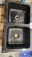 Top down view of double bowls showing drain holes and glossy black granite surface.