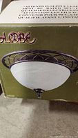 Packaging box showing globe light fixture with an antique brown metal frame and white marbleized glass dome diffuser.