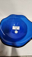Top-down view of the blue glass vessel sink showing the wavy edges, circular drain hole, and glossy translucent blue glass material.