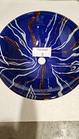 Top view of blue glass vessel sink with brown and white swirl pattern and a central drain hole.
