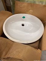 White oval under mount ceramic sink inside brown cardboard box, showing clean smooth glossy finish.