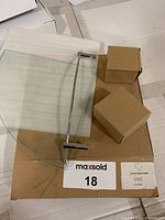 Corner glass shower shelf visible with two brown boxes containing hardware, all resting on original cardboard packaging with MaxSold label and LUX branding.