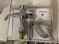 Full view of chrome bathroom faucet with pop-up drain and braided hoses on cardboard box surface.