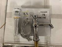 Chrome finished faucet with attached hose and pop-up drain laid on box