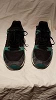 Front view of Adidas running shoes showing colourblock pattern with black, green, and hints of red, black laces tied.