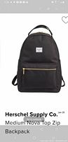 Front view of black Herschel Supply Co. Medium Nova Top Zip backpack showing the front pocket with gold-tone zipper and the brand logo patch.