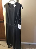 Front view of black sleeveless evening dress hanging on hanger, showing original Calvin Klein tag on side.