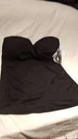 Black strapless swimwear top laid flat, showing front view with attached tag and no straps currently on.