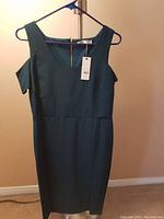 Front view of green dress hanging showing square neckline, cut out shoulder design, and fitted waist.