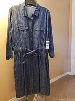 Blue print long sleeve denim pattern button down dress on hanger, front view with collar, button closure, chest flap pockets, and waist tie.