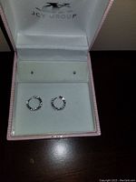 Pair of small white gold hoop earrings inside a pink JCY Group box, showing front view of both earrings.