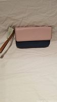 Front view of Fossil clutch showing pink flap and navy blue body with attached leather wrist strap and original tag.