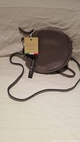 Photo showing front view of the grey round handbag with attached tags and adjustable leather strap.