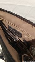 Interior view of the grey travel bag showing brand patch, multiple pockets and beige lining