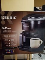 Front view of the Keurig K-Duo Essentials coffee maker box showing product image, features like 1.77L capacity, use of ground coffee or K-Cup pods, multiple brew sizes.