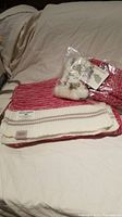 Photo showing the red and white knit scarf folded, and the mittens inside clear packaging with tags visible, placed on a neutral background.