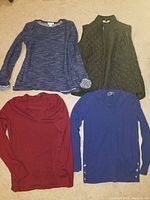 Photo showing four knit tops and one vest laid on the floor, clearly displaying their styles and colors.