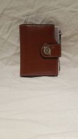 Front view of a brown faux leather ladies wallet with snap closure featuring a metallic flower detail.