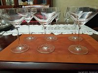 Six clear martini glasses with Schott brand label visible on the rim area, arranged on a brown placemat on a wooden table.