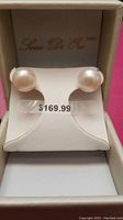 Front view of pearl earrings displayed on white holder inside box showing large round white pearls and price tag sticker of $169.99.