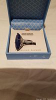 Ring with blue lapis lazuli gemstone showcased in its original blue patterned box with a product information insert.
