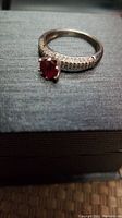Close-up photo of the sterling silver ring with red ruby center stone and clear stones on the band.
