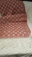Pink and white checkered soft scarf laid out flat showing pattern and fringe details.