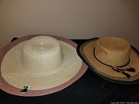 Two wide brim straw sun hats side by side. Left hat natural straw with pink rim and tagged. Right hat natural straw with black rim and black tassel tie, Saks Fifth Avenue brand.