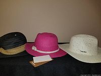 Photo showing three ladies sun hats: black with tan band, pink with white braided trim and flower, white with Calvin Klein logo.