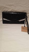 Front view of new black ladies wallet clutch with tag visible and wrist strap.
