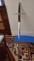 Full-length view of the sword leaning against a wall on a rug, showing overall length and condition
