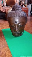 Front view of Buddha head sculpture on green background showing facial features and patina