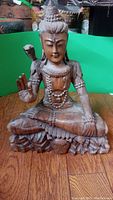 Full frontal view of the carved wooden Buddha statue with closed eyes and snake on left shoulder, seated cross-legged on carved lotus base.