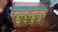 Front view showing five green panels with floral motifs and turned bun feet