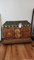 Front view of the wooden handpainted chest showing the overall decoration and top roof-like detailing with floral banding