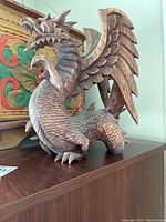 Side view of carved wooden dragon statue showing detailed scales, wings, and open mouth.