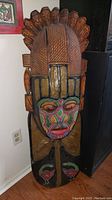 Front view of large tiki mask showing colorful facial paint and carved headdresses.